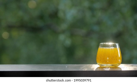 Glass full of with orange juice with jelly pieces on the brown organic wooden table with green morning summer or spring trees leaves 
bokeh background. Making drinks outdoors.