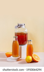 Glass gar with komucha tea, citrus fruits and two bottles with ready beverage on modern podiums in front of yellow background with copy space. Orange and lemon. Healthy fermented drink. Vertical