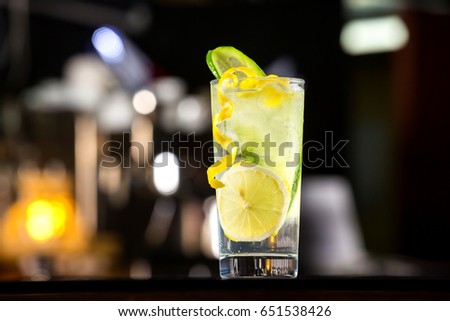 Glass of gin tonic cocktail decorated with cucumber at bat counter background.