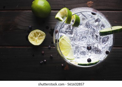 Glass of gin tonic with cucumber, lime and ice over a wooden table