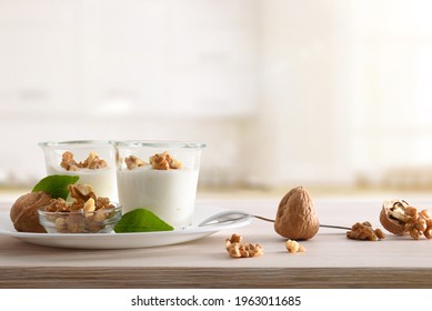 Glass Glasses With Yogurt With Walnuts And Bowl With Walnuts On Wooden Kitchen Bench. Front View.