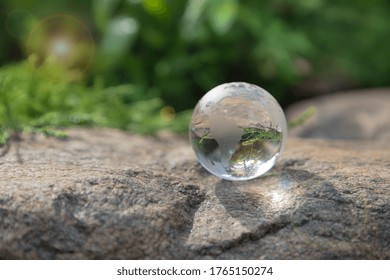 Glass globe on a stone, blurred natural background, artistic light. World Environment day concept. - Shutterstock ID 1765150274