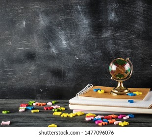 glass globe is standing on a stack of notebooks on the background of a black chalk board, copy space, concept back to school