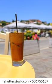 A Glass Of Greek Frappe Coffee On A Table, Closer View. At The Port Of Evdilos, Ikaria, North Aegean Islands