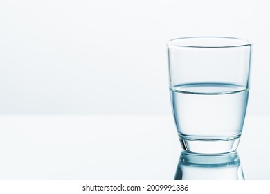 A Glass Of Half Water On Clear White Background, Half Full Or Half Empty, Contradictory Attitude And Point Of View