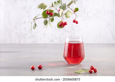  glass of hawthorn berry juice and a branch with fresh berries on a gray background - Shutterstock ID 2058600875