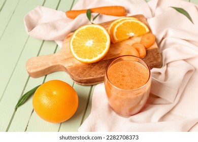 Glass of healthy orange smoothie and ingredients on green wooden table