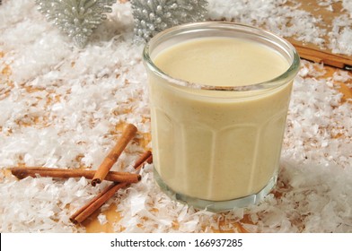 A Glass Of Holiday Egg Nog In The Snow With Christmas Ornaments And Cinnamon Sticks