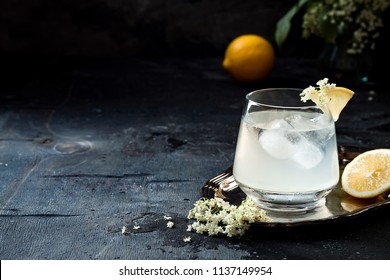 A glass of homemade elderflower gin sour or lemonade garnished with freshly picked elderflowers.