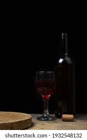 A glass of homemade wine next to a bottle on a dark background. Glass of red wine on a black background. Alcoholic drink