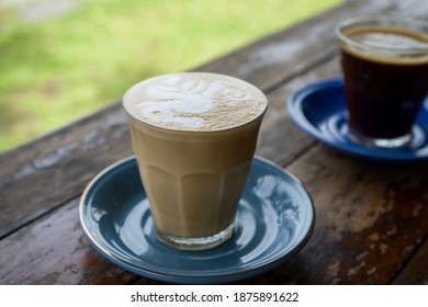 A glass of hot caffelatte with a beautiful seahorse shaped foam, close-up shots on the wooden table with blurred background.