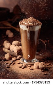 Glass Of Hot Chocolate With Whipped Cream And Truffles On An Old Brown Table. Sweets And Drink Sprinkled With Cocoa Powder.