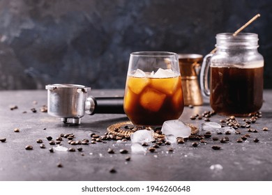 Glass Of Ice Coffee With Ice Cubes Served With Cream, Copper Cezve And Coffee Beans Over Dark Texture Background