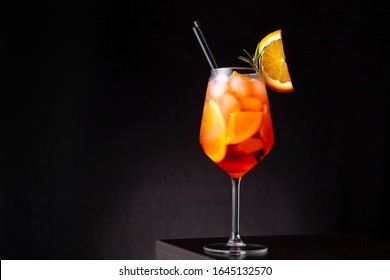 Glass of ice cold Aperol spritz cocktail served in a wine glass, decorated with slices of orange and rosemary branch, placed on a bar counter
