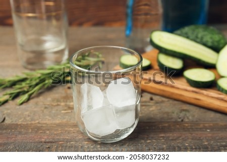 Glass with ice cubes and ingredients for gin tonic on wooden background