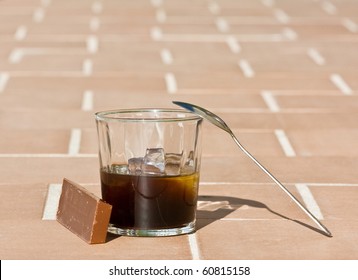 Glass of iced coffee, chocolate and a spoon resting on the glass with the bottom out of focus