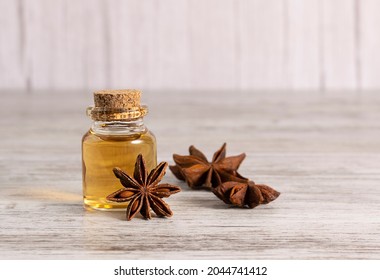 A glass jar with anise oil stands on a light wooden table. Stars of star anise with seeds in the background - Powered by Shutterstock