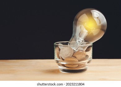 Glass Jar And Alot Of Coins, Light Bulb On Top Put On Table, Hope, Education, Home, Loan, Step To Keep Money, Save And Family Concept Isolated On Black Background.