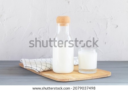 Glass jar with cork of homemade yogurt, kefir, buttermilk or natural fermented milk next to glass of milk on kitchen table. Healthy probiotic dairy drink concept