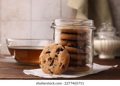 Glass jar with delicious chocolate chip cookies and tea on wooden table - Powered by Shutterstock