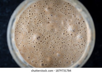 Glass jar with dough leaven. Preparing yeast dough for bread, buns, pastries or pizza, close up, top view. Cooking process