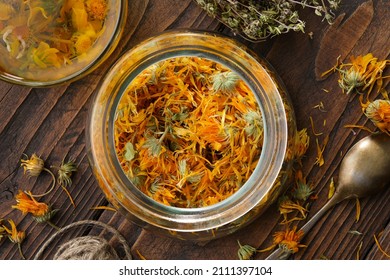 Glass jar of dried calendula flowers, cup of healthy calendula herbal tea, thyme medicinal herbs on wooden table. Top view. Alternative herbal medicine.