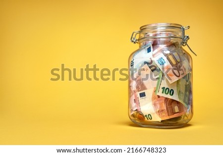 Glass jar with euro currency savings on yellow background