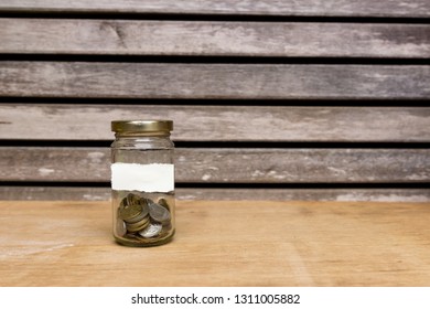 Glass jar filled with coins attached with empty white paper on wooden background. Free copy space. Financial concept.