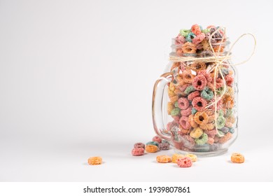 A glass jar filled with vibrant, colorful cereal rings tied with twine, placed against a clean white background. Some cereal pieces are scattered around the jar. - Powered by Shutterstock