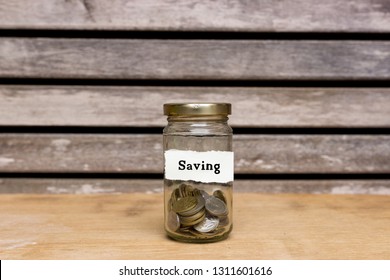 A glass jar full with coins attached with label written Saving on wooden backround. Free copy space. Saving financial concept.