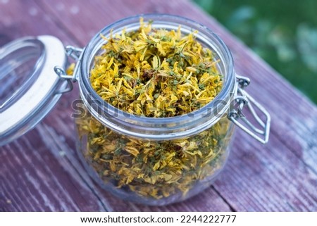 Glass jar full of dry St John's wort or Hypericum perforatum petals on old wood background. St John's wort flower herb.