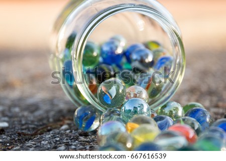 Glass jar full of marbles, fallen on the street. View of jar at an angle.
Bright picture, with blue as main color.
Front and background blurred.
Other colors red, green, yellow.