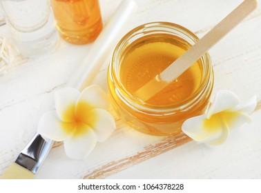 Glass jar of golden honey closep with frangipani flowers. Preparing natural beauty & body treatment at home, sweet yellow sugar nectar facial mask. 