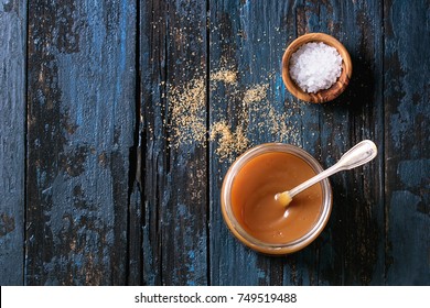 Glass jar of homemade salted caramel sauce with spoon, brown sugar and bowl of salt. Over old dark blue wooden background. Top view with space - Powered by Shutterstock