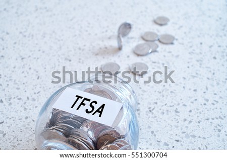 Glass jar with many coins and TFSA word over a marble counter top. Canadian Tax-Free Savings Account concept.