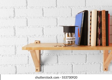 Glass Jar With Money For Education, Books And Notepads On Wooden Shelf