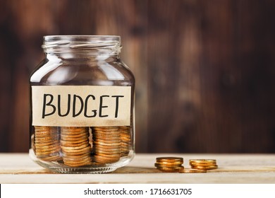 Glass jar with money and a sticker with the words BUDGET, on a wooden table.