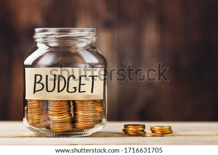 Glass jar with money and a sticker with the words BUDGET, on a wooden table.