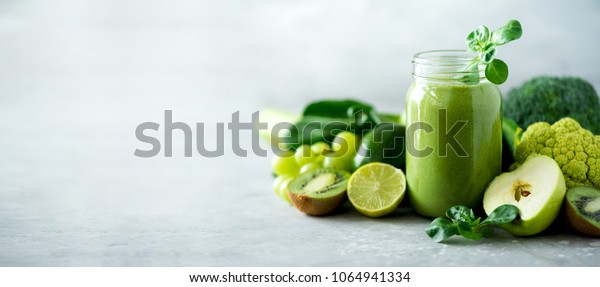 Glass jar mugs with green health smoothie, kale leaves, lime, apple, kiwi, grapes, banana, avocado, lettuce. Copy space. Raw, vegan, vegetarian, alkaline food kitchen wallpaper concept