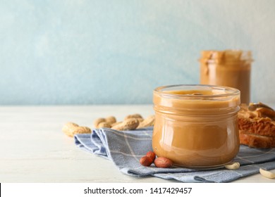 Glass jar with peanut butter, peanut, kitchen towel, spoon and peanut butter sandwich on white wooden background, space for text
