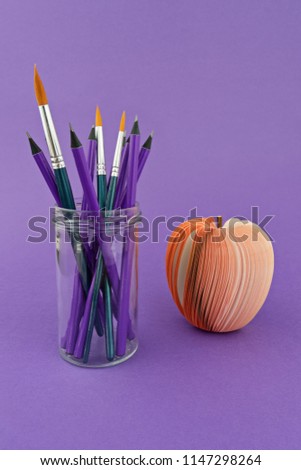 Foto Bild Glasbecher mit Stiften und Pinseln auf violettem Hintergrund