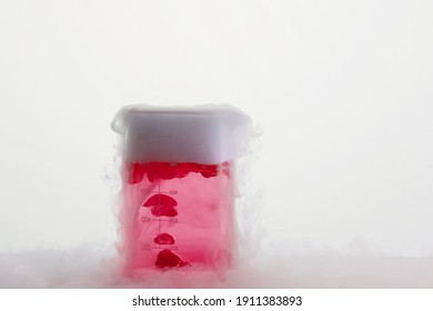 Glass Jar With Red Chemical And Smoke.  Sublimation Of Dry Ice On A White Background. Beaker On The Lab Table.