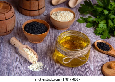 Glass Jar Of Sesame Oil, Raw White And Black Sesame Seeds, Wooden Dish, Fresh Herbs On A Wooden Background. Healthy Lifestyle. Natural And Healthy Oil.
