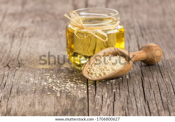 Glass jar of sesame oil and raw sesame seeds in\
wooden shovel with burlap sack on wooden table. Uncooked sesame\
background concept with copy\
space