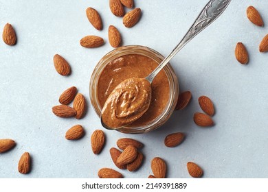 Glass Jar And Spoon Of Almond Butter On Light Gray Background, Top View, Above