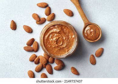 Glass Jar And Spoon Of Almond Butter On Light Gray Background, Top View, Above