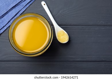 Glass jar and spoon of Ghee butter on grey wooden table, flat lay. Space for text