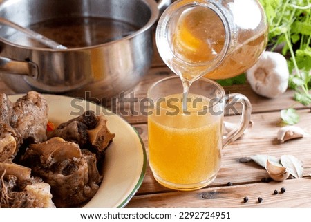 Glass jar with yellow fresh bone broth o on rustic wooden table. Healthy low-calories food is rich in vitamins, collagen and anti-inflammatory amino acids