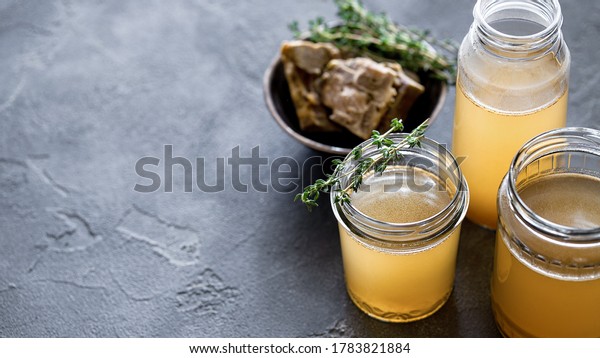Glass jar with yellow fresh\
bone broth on dark gray background. Healthy low-calories food is\
rich in vitamins, collagen and anti-inflammatory amino\
acids