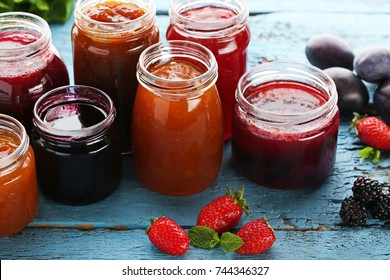 Glass jars with different kinds of jam and berries on wooden table